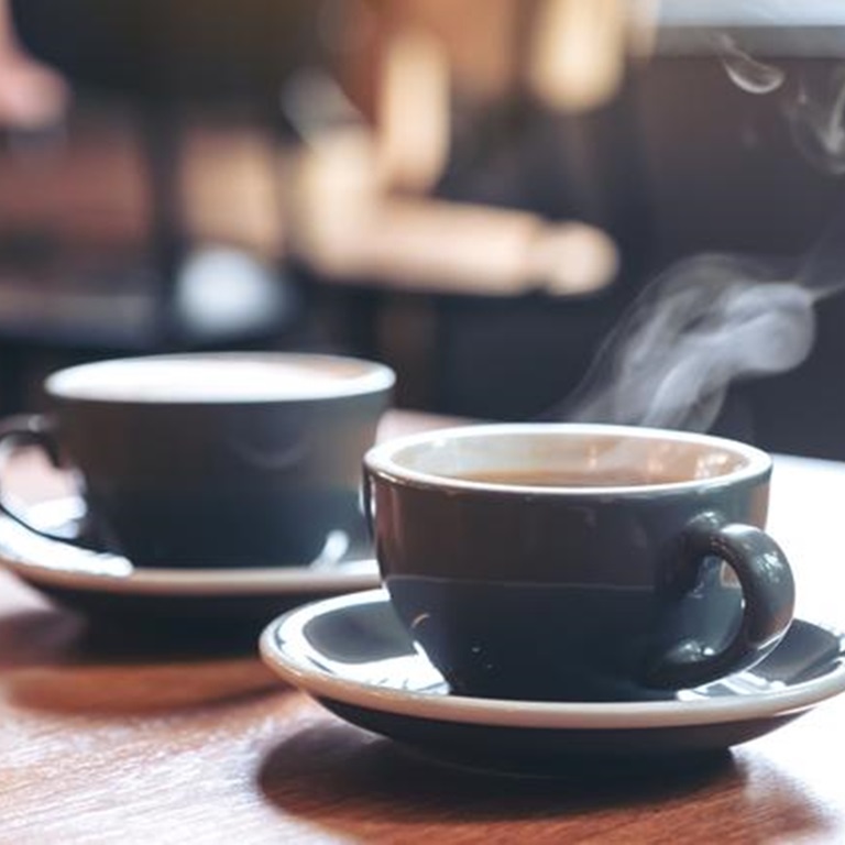 Two coffee cups on a table, one steaming