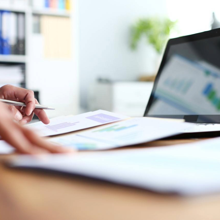 Papers with charts and graphs on a desk in front of a laptop in an office setting.