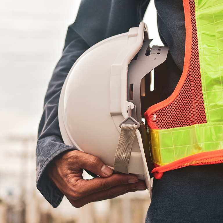 A construction worker holding a safety helmet while wearing a reflective vest, symbolising the importance of safety and risk management in fleet operations.