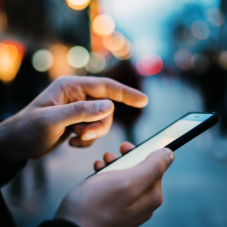 Closeup of male hands typing an sms message via smartphone outside, hipster man enjoying evening walk and using his cellphone, bokeh lights