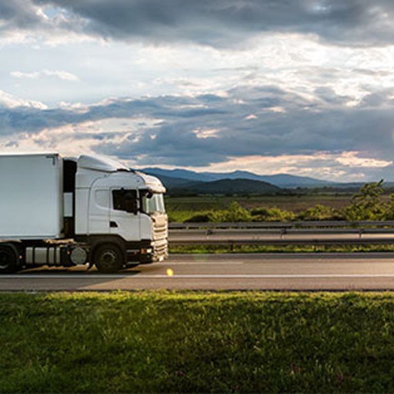 White lorry traveling on main motorway with green fields either side and clouds above