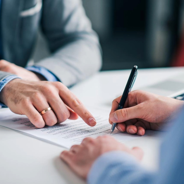Close-up of two people's hands pointing out where to sign and signing an agreement.